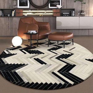 May include: A large circular area rug featuring a geometric herringbone pattern composed of individual rectangular tiles in contrasting shades of black, white, and grey, creating a textured visual effect across the entire round surface.
