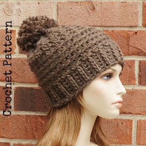 May include: A brown knitted beanie with a fluffy pom pom on top. The beanie is worn by a mannequin with long brown hair.