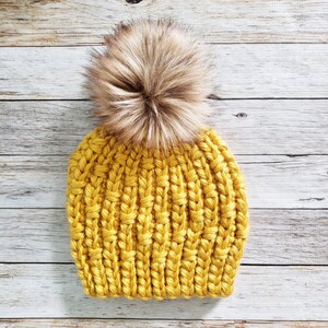 May include: A yellow knitted beanie with a brown faux fur pom pom.