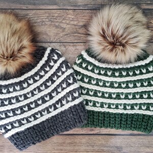 May include: Two knitted winter hats with white and grey stripes and white and green stripes. Both hats have a faux fur pom pom on top.