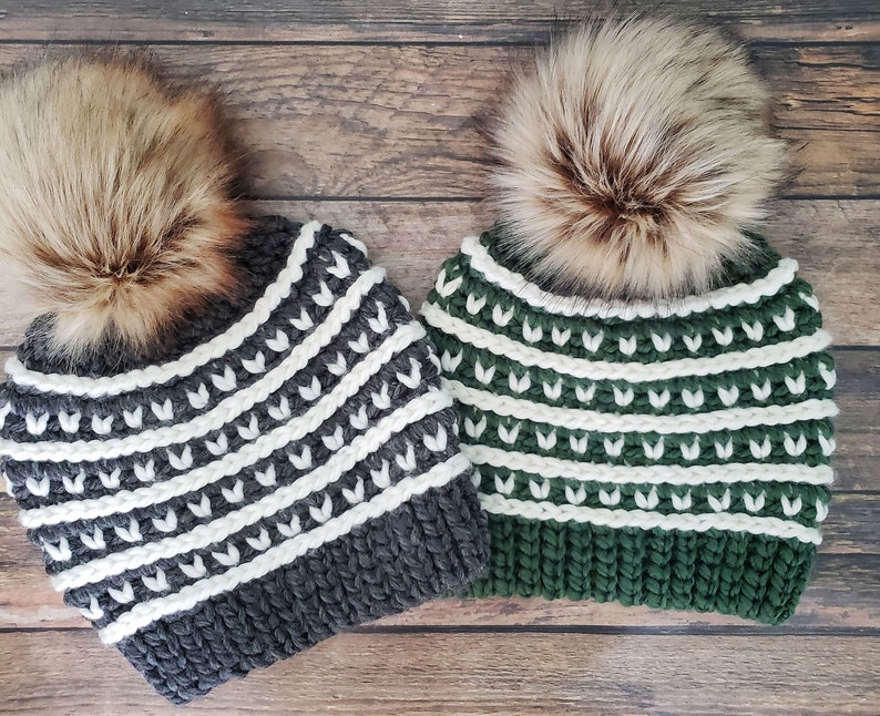 May include: Two knitted winter hats with white and grey stripes and white and green stripes. Both hats have a faux fur pom pom on top.