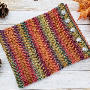 Op de afbeelding: Een veelkleurige gebreide nekwarmer met een textuurpatroon en zilveren knopen.