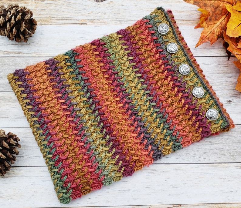 Op de afbeelding: Een veelkleurige gebreide nekwarmer met een textuurpatroon en zilveren knopen.