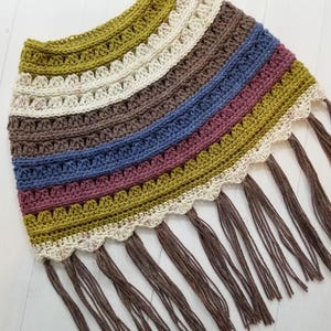 May include: A crocheted poncho with a scalloped edge and fringe in shades of green, brown, cream, blue, and pink.