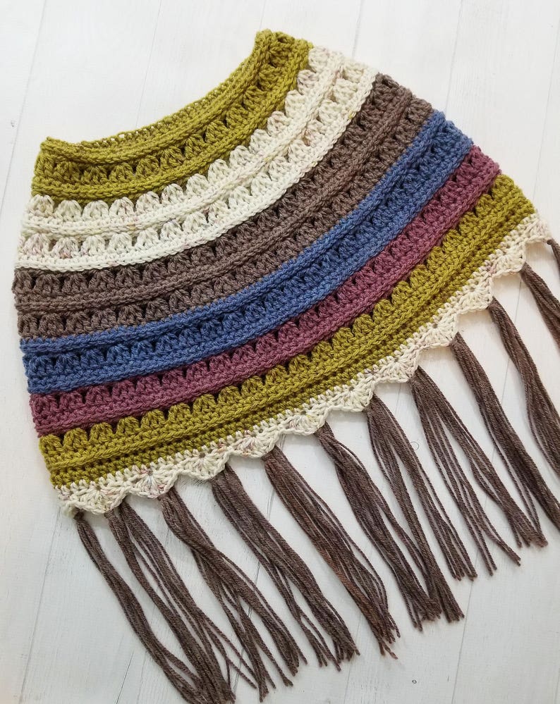 May include: A crocheted poncho with a scalloped edge and fringe in shades of green, brown, cream, blue, and pink.