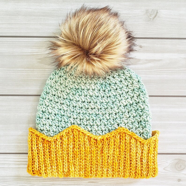 May include: A crocheted beanie hat with a yellow brim and a fluffy brown pom pom on top. The hat is made with a light green and white yarn.