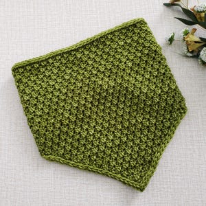 May include: A handmade, olive green crochet cowl. The cowl is square-shaped with a textured stitch pattern and a solid border. The item is displayed on a neutral surface, showcasing the handmade craftsmanship and the rich color of the yarn.