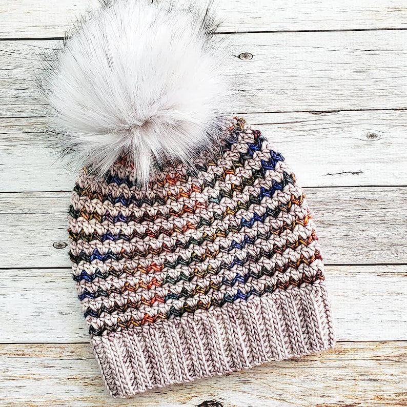 May include: A crocheted beanie with a colorful chevron pattern and a white faux fur pom pom. The beanie is made with a soft, warm yarn and is perfect for keeping your head warm in the winter.