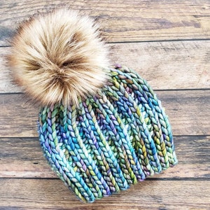 K&ouml;nnte beinhalten: Eine blaue, gr&uuml;ne und violette Strickm&uuml;tze mit einem braunen Kunstfellbommel.