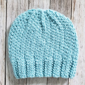 May include: A light blue knitted beanie hat. The hat is made with a chunky yarn and has a simple, classic design.