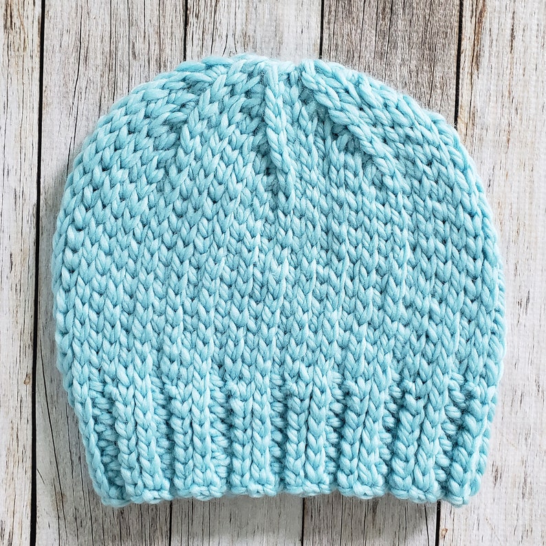 May include: A light blue knitted beanie hat. The hat is made with a chunky yarn and has a simple, classic design.