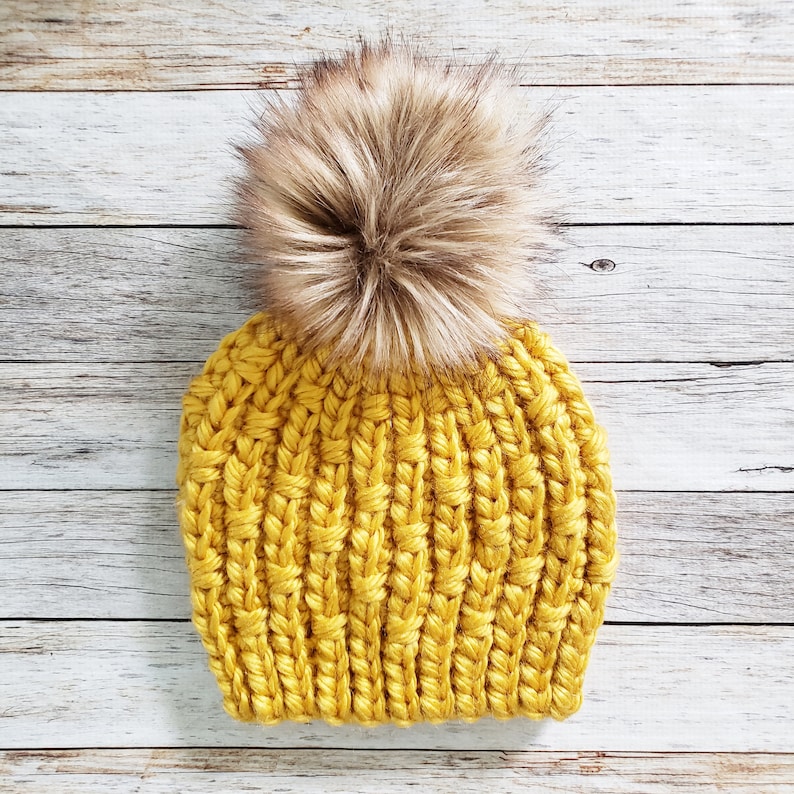 May include: A yellow knitted beanie with a brown faux fur pom pom.
