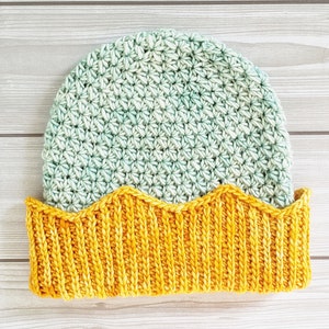 May include: A crocheted hat with a green and white ombre design and a yellow knit brim. The brim has a scalloped edge.