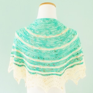 Könnte beinhalten: Ein gehäkeltes Tuch in Teal- und Weißtönen mit einem gewellten Rand. Das Tuch wird auf einer weißen Schaufensterpuppe präsentiert.