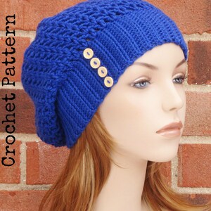 May include: A blue crocheted beanie with a textured stitch pattern and four wooden buttons. The beanie is worn by a mannequin with long, light brown hair.