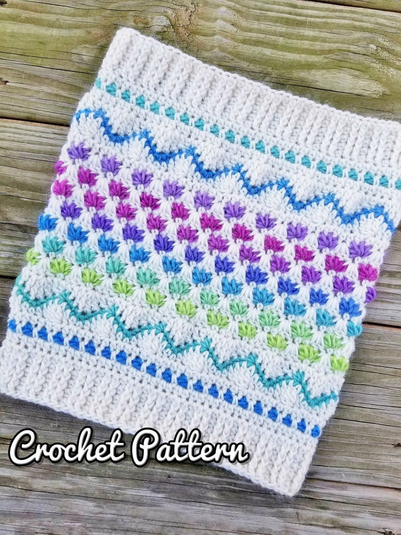 May include: A crochet pattern for a colorful cowl with a white background and a wavy blue, green, and purple design. The text "Crochet Pattern" is written below the cowl.