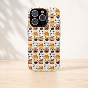 May include: A phone case featuring a repeating pattern of Halloween-themed icons on a cream background. The design includes orange pumpkins with bows, white ghosts, yellow and orange candy corn, and cupcakes with sprinkles and small bats.