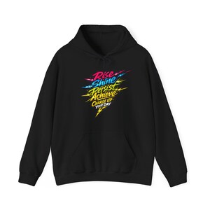 May include: Black hoodie with a front pocket and drawstring hood. The front features the text "Rise, Shine, Persist, Achieve, Charge Up Your Day" in a colorful, stylized design with lightning bolt accents. A casual, comfortable garment.