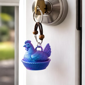May include: A blue and purple iridescent chicken keychain hanging from a key in a door lock. The chicken is sitting in a woven basket. The keychain has a brown leather strap with wooden beads.