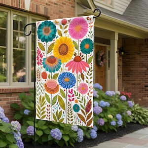 May include: A colorful garden flag featuring a vibrant floral design. The flag showcases a variety of flowers in shades of pink, yellow, blue, and teal, set against a white background. Green leaves and stems complete the botanical theme, perfect for outdoor decor.