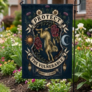 May include: A dark blue garden flag with a central design featuring a golden hare surrounded by roses, a sun, and a crescent moon. The text reads "PROTECT THE VULNERABLE, RESIST TYRANNY". Decorative elements include thistles and lanterns.