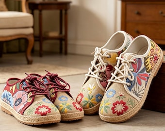 Könnte beinhalten: Zwei Paar flache Sneaker mit einer Basis aus strukturiertem beigem Stoff und lebendiger Blumenstickerei in Rot-, Blau-, Gelb- und Grüntönen. Die Schuhe haben dicke weiße Seilschnürsenkel und eine geflochtene Jutekante an den Gummisohlen.