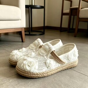 K&ouml;nnte beinhalten: Ein Paar wei&szlig;e Mary Jane-Schuhe aus Spitze mit floralen Verzierungen. Die Schuhe haben eine gewebte Jutesohle und einen Riemen &uuml;ber dem Oberteil. Schuhgr&ouml;&szlig;e 39.