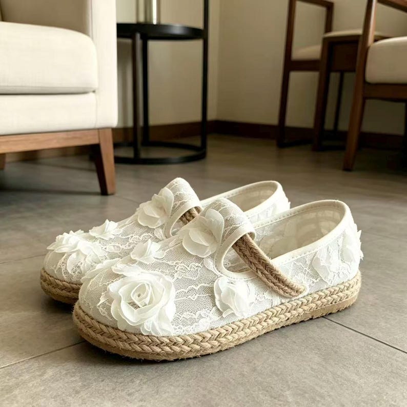 K&ouml;nnte beinhalten: Ein Paar wei&szlig;e Mary Jane-Schuhe aus Spitze mit floralen Verzierungen. Die Schuhe haben eine gewebte Jutesohle und einen Riemen &uuml;ber dem Oberteil. Schuhgr&ouml;&szlig;e 39.