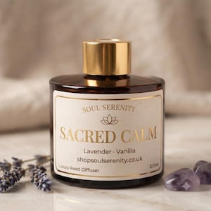 May include: A brown glass reed diffuser bottle with a gold cap and a cream label. The label reads SOUL SERENITY, SACRED CALM, Lavender, Vanilla, shopsoulserenity.co.uk, and 100ml. Dried lavender sprigs and two purple stones sit beside the bottle.