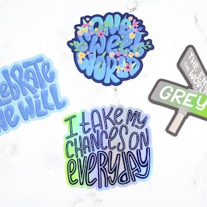 May include: Four colorful stickers with different phrases. The first sticker is blue and says "Celebrate We Will". The second sticker is blue and says "One Sweet World" with flowers around the text. The third sticker is blue, green, and purple and says "I Take My Chances On Everyday". The fourth sticker is green and gray and says "The End of the World Grey St."