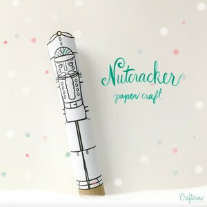 Puede incluir: Una plantilla de artesanía de papel imprimible de un cascanueces. La plantilla es en blanco y negro y se puede colorear. La plantilla está enrollada en forma de tubo. El texto "Nutcracker paper craft" está escrito en cursiva verde.