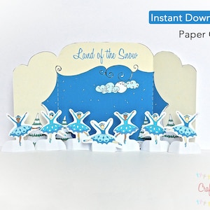 May include: Paper craft kit featuring a winter scene with ballerinas in blue tutus and a backdrop of a blue sky with clouds. The title "Land of the Snow" is printed on the front of the craft.