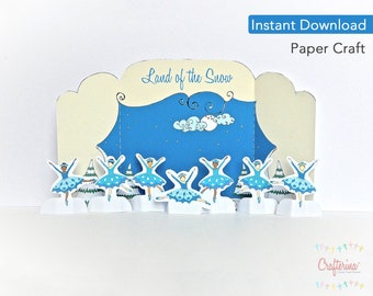 May include: Paper craft kit featuring a winter scene with ballerinas in blue tutus and a backdrop of a blue sky with clouds. The title "Land of the Snow" is printed on the front of the craft.