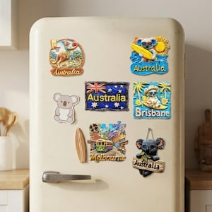 Puede incluir: Una colección de nueve imanes decorativos para nevera con temas australianos, que incluyen un canguro jugando al baloncesto, koalas surfeando, la bandera de Australia, un tranvía de Melbourne y un koala sosteniendo un cartel que dice Australia.