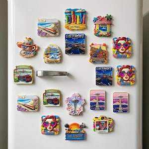 Könnte beinhalten: Eine Sammlung farbenfroher Souvenir-Kühlschrankmagnete mit Darstellungen von Las Vegas, Detroit, Hawaii, Seattle und Los Angeles. Die Magnete zeigen Wahrzeichen, Stadtansichten und stilisierte Porträts.