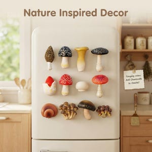 May include: A set of eleven assorted mushroom-shaped magnets arranged on a cream-coloured refrigerator. The magnets feature various species including morel, fly agaric, and chanterelle designs. A note reads: Nature Inspired Decor. Foraging notes: Add Chanterelle to Omelet!