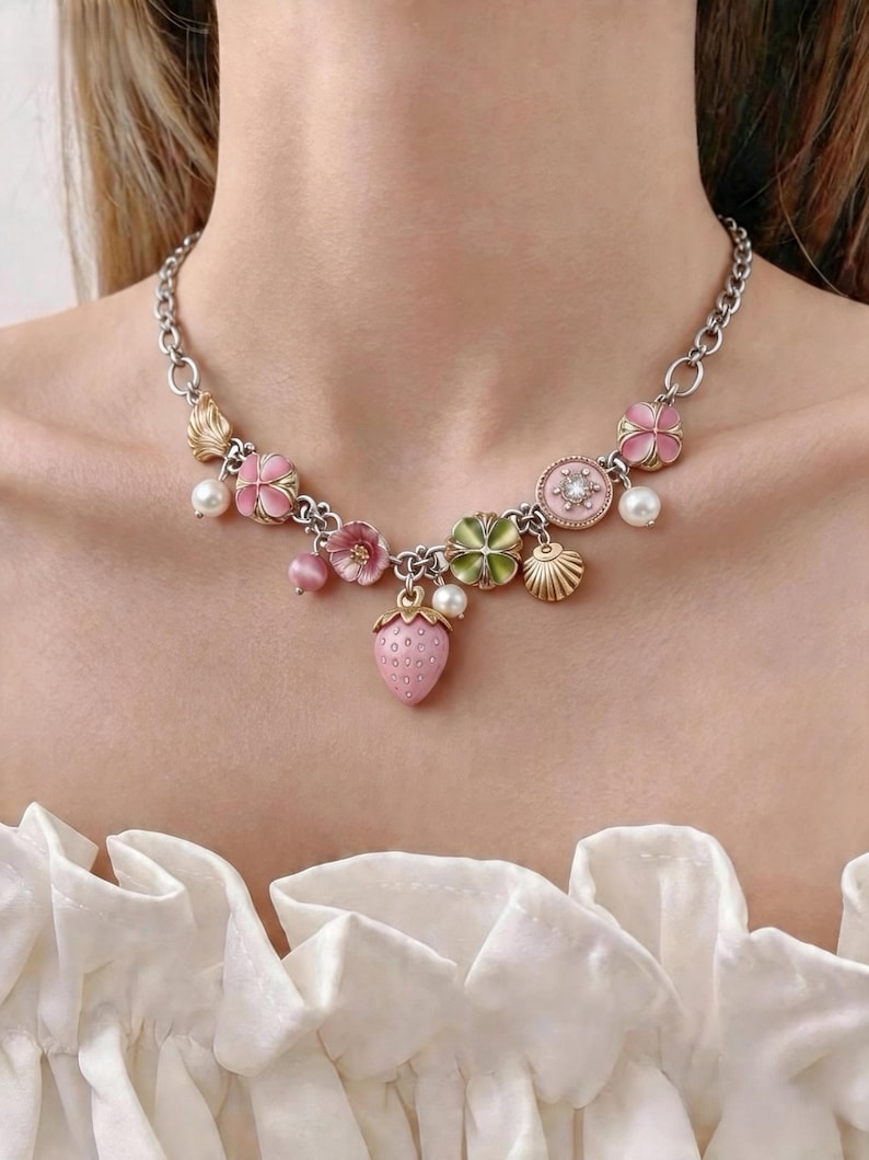 May include: Silver-toned necklace featuring pink flower, strawberry, and seashell charms. The necklace includes faux pearls and gold-toned accents. The chain is a linked design, and the necklace is worn around the neck.