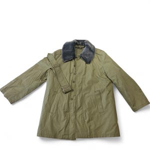 Może przedstawiać: Oliwkowy płaszcz w stylu wojskowym z szarym kołnierzem ze sztucznego futra. Płaszcz ma zapinany na guziki przód, dwie kieszenie i pasek na ramię. Płaszcz jest wykonany z wytrzymałej tkaniny.