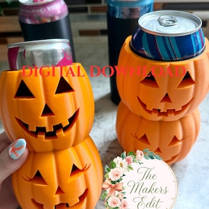 May include: Two orange 3D-printed pumpkin-shaped beverage can holders, each featuring a carved jack-o'-lantern face with triangular eyes and a jagged mouth. The text DIGITAL DOWNLOAD is visible in red, along with a floral logo for The Makers Edit.