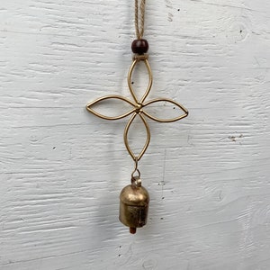 May include: A gold metal wind chime with a flower design and a bell hanging from the bottom. The chime is suspended from a brown twine cord.