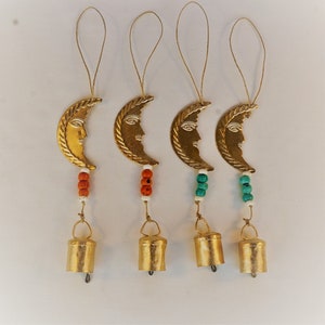 Może przedstawiać: Cztery złote wiatraczki w kształcie półksiężyca z koralikami i dzwonkami. Półksiężyce mają wzór twarzy. Dwa wiatraczki mają turkusowe koraliki, a dwa mają pomarańczowe koraliki.