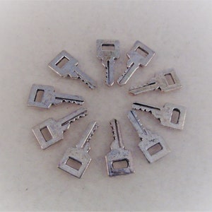 May include: A collection of ten silver keys arranged in a circle on a white surface.