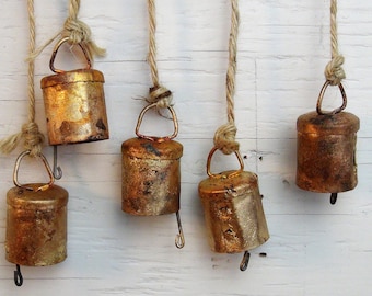 May include: Six small, gold-colored bells hanging from twine. The bells are slightly tarnished and have a rustic look.