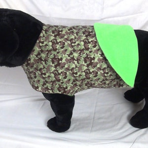 May include: A black dog wearing a camouflage dog vest with a bright green patch on the back.
