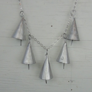May include: A silver chain with five silver bells hanging from it. The bells are cone-shaped and have a hammered texture.