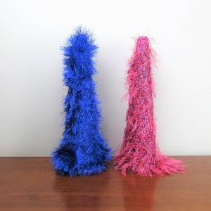 May include: Two decorative cone-shaped trees, one blue and one pink, with a fuzzy texture, standing on a wooden surface.
