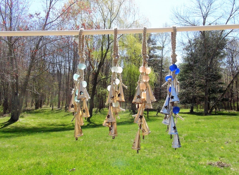 May include: A set of six wind chimes with different colored glass beads and star-shaped bells. The chimes are made of metal and have a rustic, natural look.