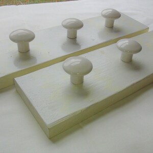 Puede incluir: Dos tablas de madera blancas con pomos de cerámica blanca. Las tablas están unidas y tienen una mancha de color amarillo claro.