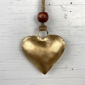 May include: A gold heart-shaped metal ornament hanging from a brown wooden bead and twine.