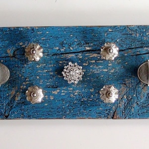 Puede incluir: Una tabla de madera azul desgastada con varios pomos y tiradores de plata y vidrio unidos. La tabla es una pieza de decoración rústica para el hogar.